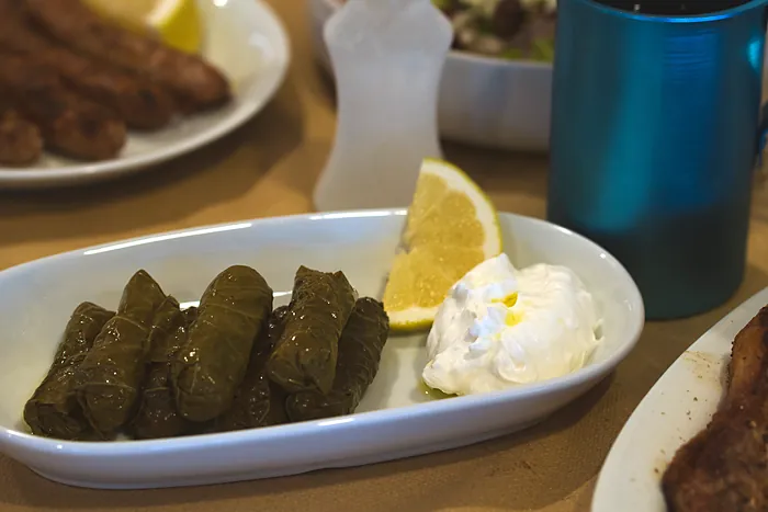 Ντολμαδάκια στο τραπέζι, δίπλα σε μπλε κανάτα κρασιού